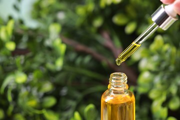 Woman dripping essential oil from pipette into bottle outdoors, closeup. Space for text