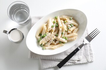 Delicious pasta with green peas, creamy sauce, water and fork on white table, top view