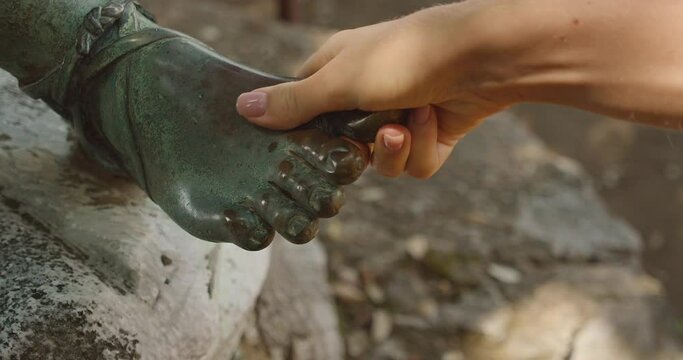 A hand carefully grasps the toes of a bronze statue's foot, symbolizing good luck and tradition.