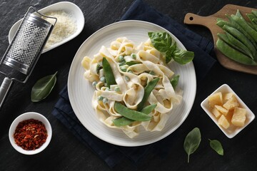 Delicious pasta with green peas and ingredients on black table, flat lay