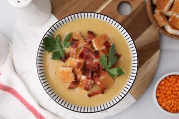 Delicious lentil soup with bacon and parsley in bowl on white table, flat lay