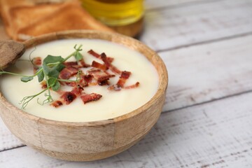 Delicious potato soup with bacon and microgreens in bowl on wooden table, closeup. Space for text