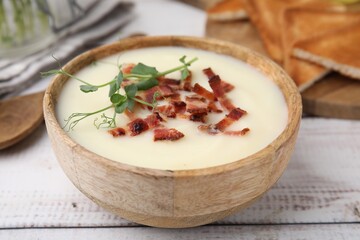 Delicious potato soup with bacon and microgreens in bowl on wooden table, closeup