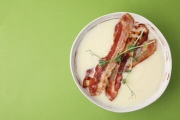 Delicious potato soup with bacon and microgreens on green background, top view. Space for text