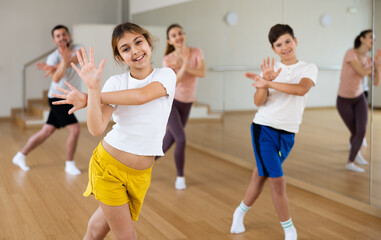 Portrait of happy preteen girl practicing dynamic synchronous choreography with her family in...