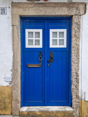 Traditional wooden door painted in vibrant blue with vintage knockers and two small hatches on top....