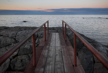 Obraz premium An old wooden bridge pier on the background of a beautiful sunset sky on the shore of the lake. Karelia, Russia.