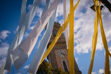 Yellow and blue fabric ribbons flutter in the wind against the background of a blue sky and an ancient clock tower