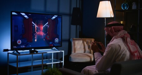 Arabic man playing singleplayer videogames on TV, relaxing in living room. Middle Eastern gamer enjoying science fiction shooter game on gaming console, having fun, handheld camera shot