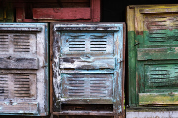 Old beehives in rustic appearance with peeling paint and chipped wood in green, blue in worn and...