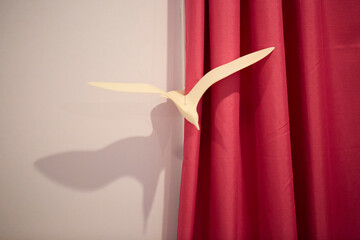 Carved white bird sculpture in front of a rich red theatre curtain.