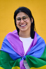 Vertical. Portrait young smiling lesbian rainbow flag on shoulders isolated yellow background. Happy homosexual and bisexual people pose cheerful looking at camera for studio photo. LGBT pride concept
