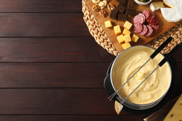 Fondue with tasty melted cheese, forks and different snacks on wooden table, top view. Space for...