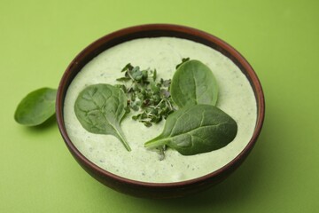 Delicious spinach cream soup with fresh leaves and microgreens in bowl on green background