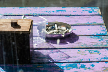 Ashtray with cigarette butts and empty plastic cup on small table near cafe
