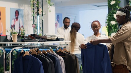African american man in fancy fashion boutique helped by employee to find suiting stylish formal...
