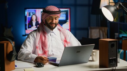 Arabic man doing online shopping, carefully typing credit card information on computer. Muslim...