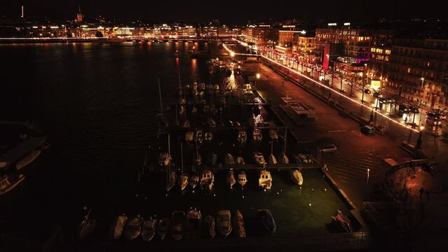 Aerial view of Geneva harbor at night, capturing boats docking, city lights and reflections on lake Geneva's waters