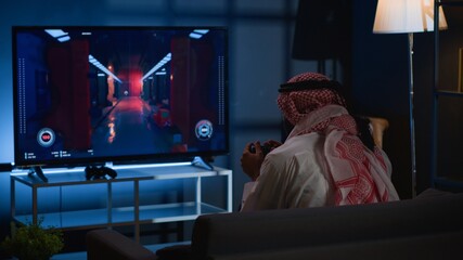 Arab man playing videogames on TV, relaxing after long day at work. Competitive gamer having fun on...