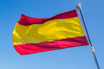 Spanish flag flying on the mast of a ship with a blue sky.