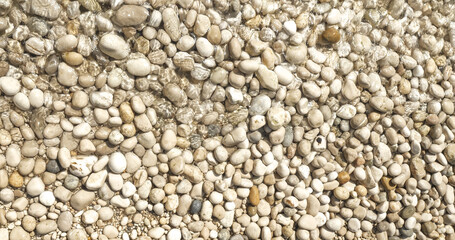 CLOSE UP: Soothing summer scenery with crystal clear water spilling over stones. Small sea waves gently splash against shore covered with white pebbles. Mesmerizing and meditative feel from the beach.