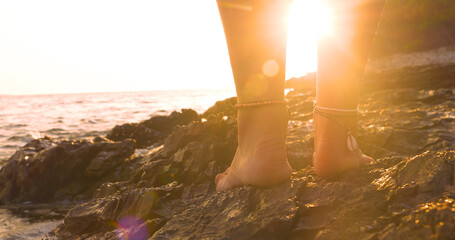 LENS FLARE, CLOSE UP: Young barefoot lady stands on a seashore where the golden rays of setting sun...