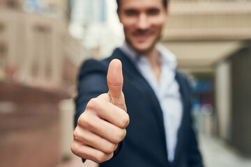 Businessman, hand and vote with thumbs up in city for review, winning or business success. Closeup...