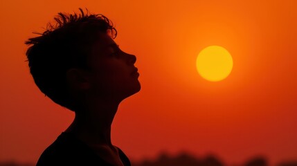 Silhouette of a young man against an orange sunset backdrop