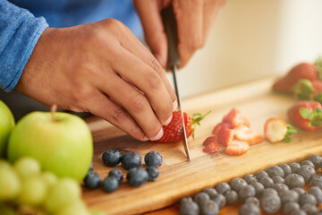 Fruits, hands and healthy food for breakfast salad with knife and cutting board in kitchen. Person or nutritionist with strawberry for wellness, diet and detox with vegan and organic recipe at home