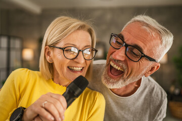 Mature wife and husband hold microphone and sing together karaoke