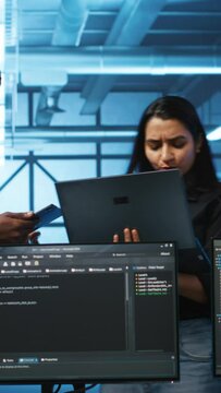 Vertical video Technician and team leader in server farm looking for equipment misconfigurations affecting performance. Multiethnic coworkers checking data center infrastructure bottlenecks leading to