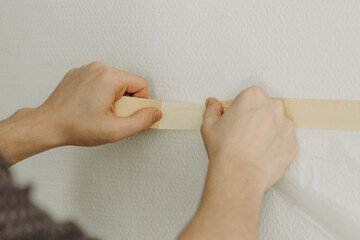 A young man puts adhesive tape on the wall.