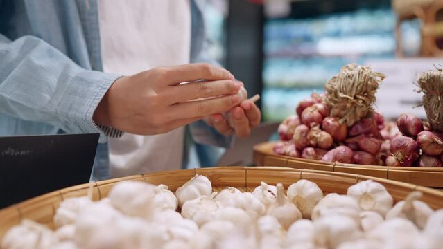 A person is holding garlic in a store. The garlic is in a basket and there are many other baskets of garlic in the store