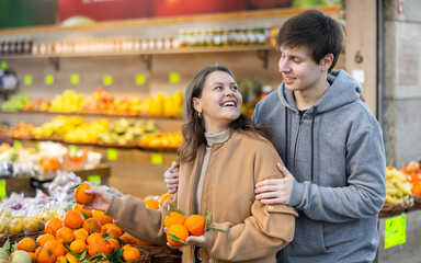 Pleased young guy and girl choosing tangerines in grocery store with large assortment
