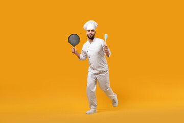 Professional chef with pan and spatula having fun on yellow background