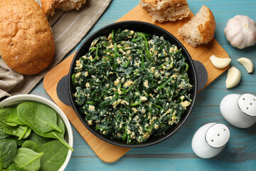 Tasty spinach dip with eggs in dish served on light blue wooden table, flat lay