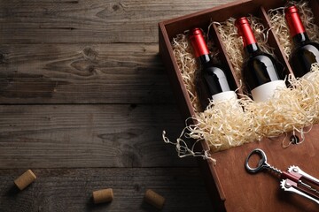 Box with wine bottles, corkscrew and corks on wooden table, flat lay. Space for text