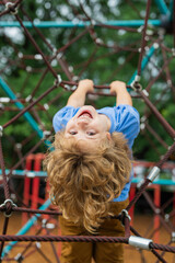 The child is hanging upside down on the playground equipment. The outdoor playground for children...