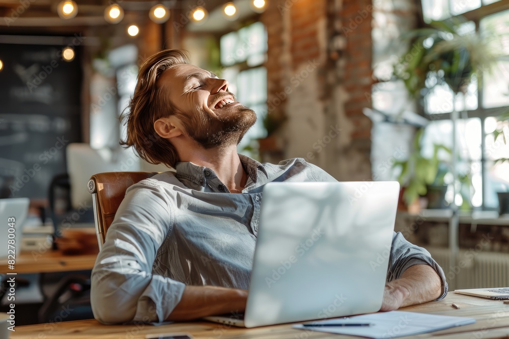 Poster a man is sitting at a desk with a laptop and smiling. he is in a happy mood and seems to be enjoying