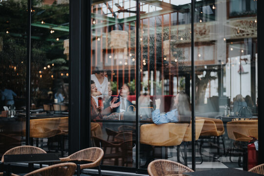 Group of friends having a lively discussion while enjoying coffee in a trendy cafe. Captured through the window, the scene reflects a cozy and lively setting.