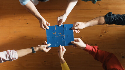 Top down view of skilled business people assemble blue jigsaw puzzle on meeting table. Group of...