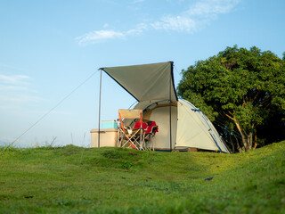 Cream Dome tent pitched on grassy field, mountainside grass field with a few trees in background....