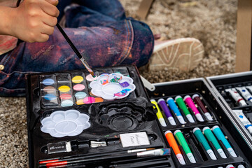 Beautiful little girl with Down syndrome painting on canvas outdoors in a sandbox in a public park...