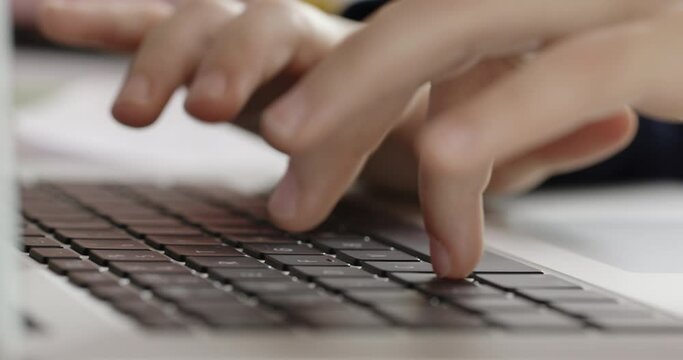 Childs hands actively typing on a laptop keyboard, focusing on finger movement and keys in a close-up shot.