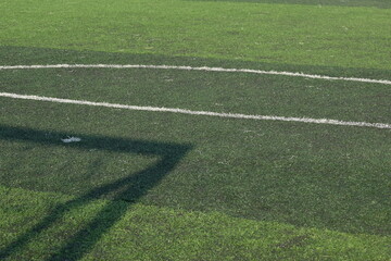 artificial green grass turf sport soccer field with black rubber granules infill and shadow of football goal