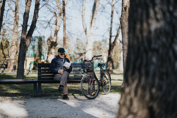 An elderly gentleman enjoys a peaceful moment reading on a sunny day in the park, with his bike parked beside him, embodying relaxation and retirement.