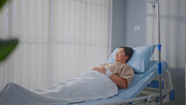 Asian mature female patient getting saline solution in hospital ward.