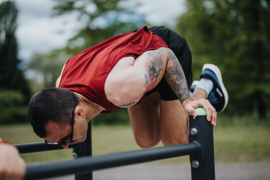 Focused male athlete, dressed in workout gear, showcasing strength and flexibility while exercising on parallel bars in a serene park environment.