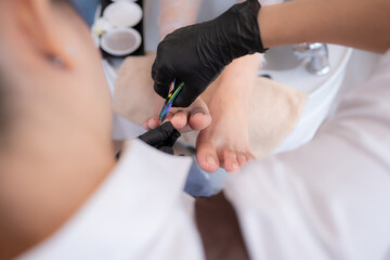 A nail technician is using tools to cut and polish foot of a customer.