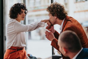 Business colleagues having a friendly greeting in a casual office setting. A man is kissing a...